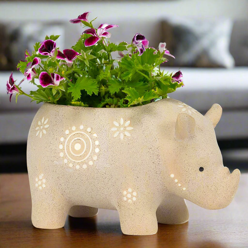 ivory colored ceramic rhino planter with flowers inside standing on coffee table with living room sofa in background